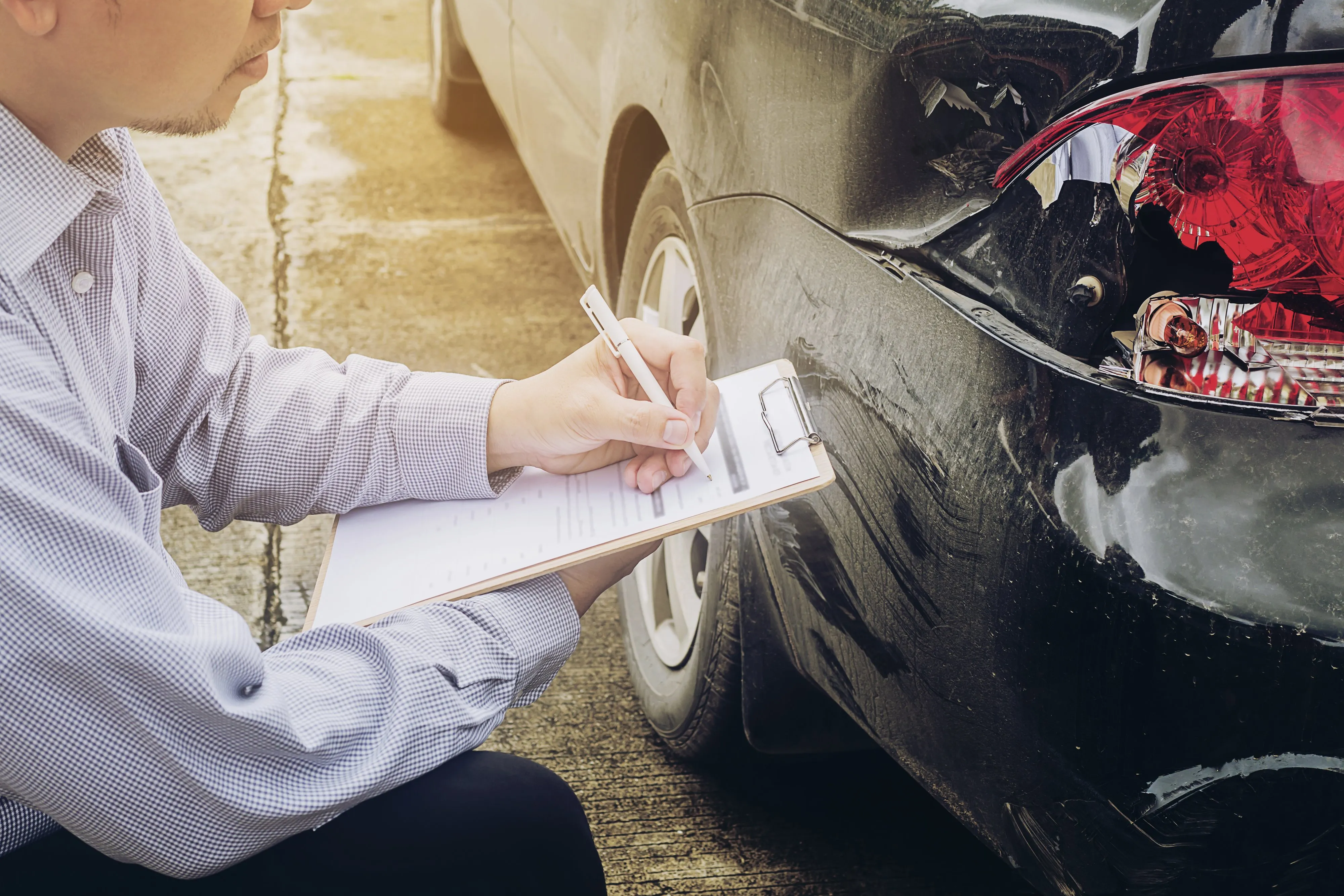 Staff examining damaged car and writing notes on clipboard